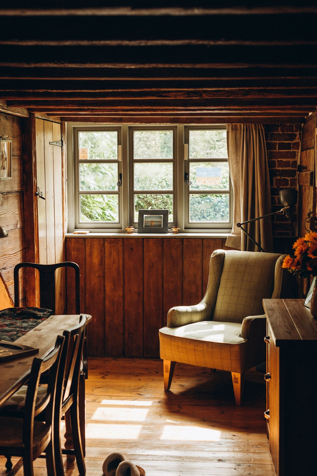 A West Cork cottage parlour with exposed beams, pine panelling and a green armchair in afternoon light