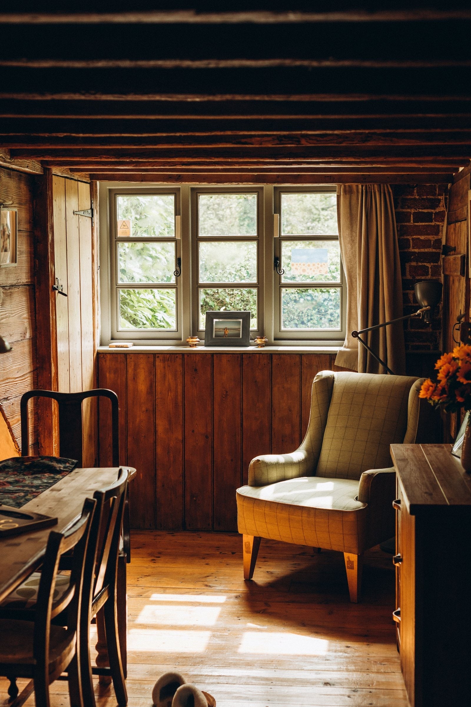 A West Cork cottage parlour with exposed beams, pine panelling and a green armchair in afternoon light
